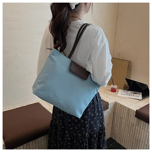 Detail of sky blue nylon tote bag with brown leather flap showing brand embossing
