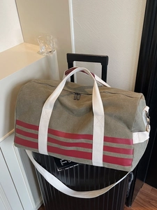 Olive green canvas travel duffel bag with red stripes resting on top of a black suitcase