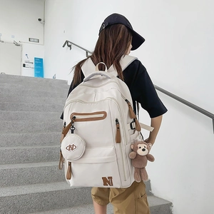 Detailed view of the creamy white large travel backpack with a plush monkey charm accessory