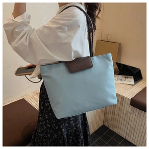 Detail of light blue nylon tote bag with brown leather handles in urban casual setting