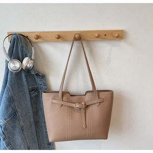 Detail view of large beige tote bag with pebbled leather texture and metal buckle