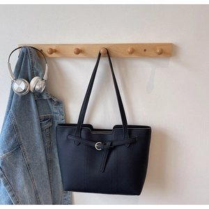 Detail of black tote bag showing lychee leather texture and golden buckle on wooden hooks