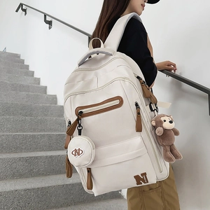 Detail of white canvas backpack featuring plush monkey charm and multiple compartments