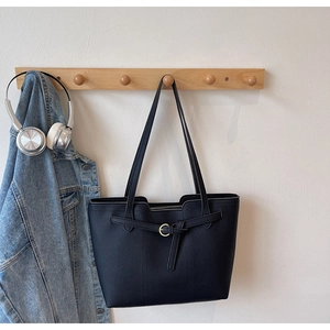 Detail of black tote bag with lychee texture leather and golden metal buckle decoration
