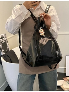 Glossy black patent leather backpack with cute white cat charm shown in a lifestyle setting