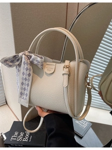 Chic white leather bucket bag with top handle, adjustable strap, and silk scarf detail