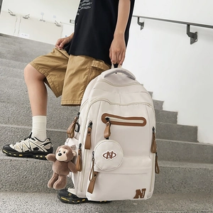 Outdoor shot of a beige large capacity backpack with a brown monkey plush pendant