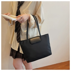 Close-up of black waterproof nylon tote bag with leather flap and embossed minimalist detail