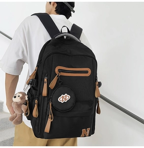 Detail of black canvas backpack with brown leather zip pulls and cute plush accessories