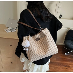 Detail view of striped canvas tote bag with brown leather strap and plush cloud pendant