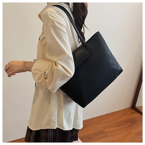 Detailed view of the large black tote bag worn with a white shirt and plaid skirt