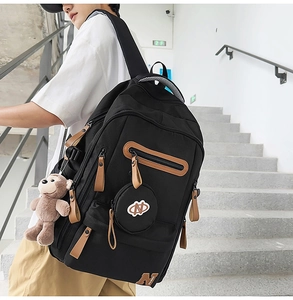 Detailed side view of black canvas backpack with brown leather accents and plush monkey charm