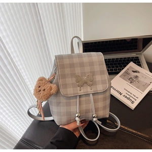 Détail d'un sac à dos à carreaux gris avec papillon argenté et pendentif ours en peluche