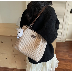 Detail of striped woven tote bag with brown leather straps and a plush bear charm