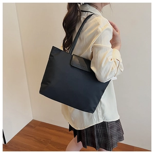 Detail of a black tote bag with leather flap and embossed text on a casual shoulder bag
