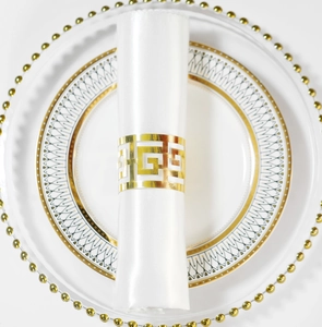 Détail d'un rond de serviette doré avec motifs grecs sur une vaisselle blanche élégante