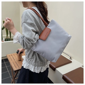 Detail of grey tote bag with brown leather straps and front flap showing the logo