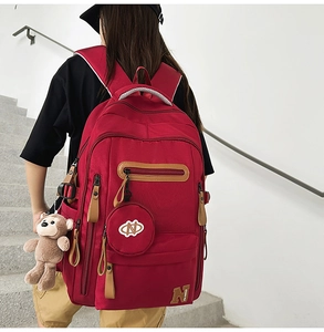 Detailed view of red large capacity backpack with teddy bear charm on model back