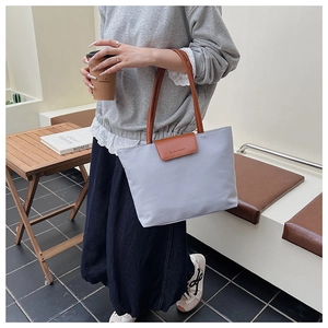 Close-up of a light gray nylon tote bag featuring brown leather flap with GLEANER logo
