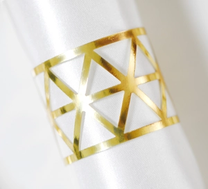 Detail of golden geometric napkin ring with hollow triangular laser cut pattern on white satin