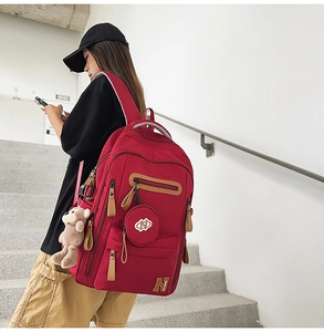 Side view of red canvas backpack with plush bear charm and detachable mini round pouch