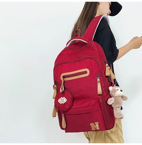 Detail of red canvas backpack showing zipper compartments and brown leather pullers