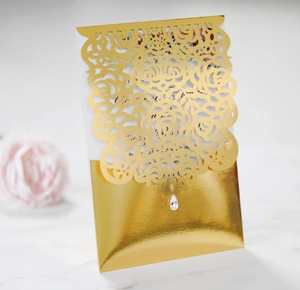 Detail of laser-cut gold rose invitation card with a teardrop crystal on marble surface