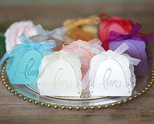 Close-up of laser-cut lace candy boxes with Love text and ribbons on a glass tray