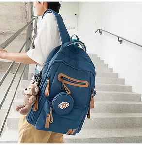 Outdoor shot of large navy blue nylon backpack with leather details and monkey keychain
