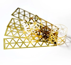 Detail of gold metal napkin ring showing geometric hollow pattern and flat-to-curled shape