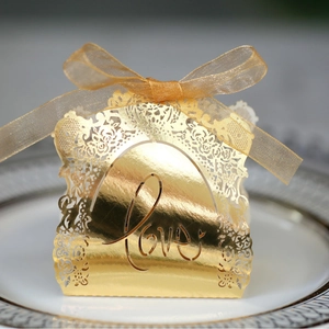 Laser-cut gold hollow LOVE candy box for weddings with ribbon bow on white ceramic plate