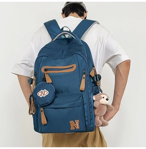 Detail of dark blue travel backpack with brown leather pulls and plush monkey charm