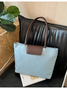 Light blue large capacity tote bag with brown flap and handles on a leather chair