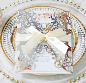 Detail of laser-cut silver wedding invitation with cream ribbon bow on a decorative plate