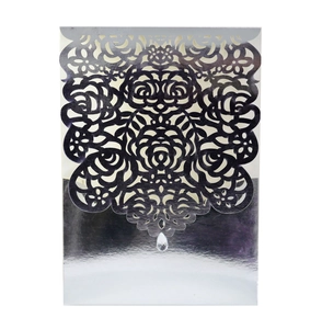 Detailed laser-cut silver mirror invitation envelope with intricate floral patterns and pendant