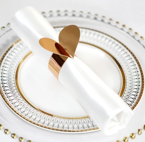 Vue macro d'un rond de serviette cœur or rose sur serviette blanche et assiette décorée