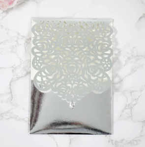 Detail of silver laser-cut rose hollow wedding invitation with a centered crystal droplet