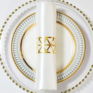 Golden hollow triangle metal napkin ring on white satin fabric and elegant plate