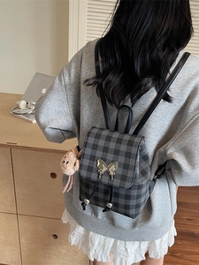 Sac à dos à carreaux avec fermoir papillon et charme en peluche sur un bureau en bois