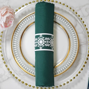 Detailed view of a white laser-cut snowflake napkin ring on a dark green fabric napkin