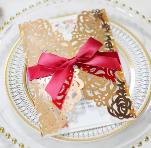 Invitation mariage dorée découpée laser avec nœud rouge sur une assiette élégante