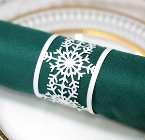 Macro shot of a white laser-cut snowflake napkin ring on a dark green cloth napkin