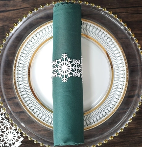 Detail of white snowflake napkin ring and dark green scalloped cloth on a plate