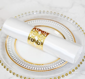 Close-up of laser-cut gold napkin ring with hollow scroll pattern on white silk
