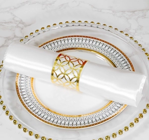 Detalle de un servilletero dorado calado con diseño geométrico sobre seda blanca fina