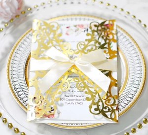 Detail of rose gold laser cut wedding invitation with cream satin ribbon on plate