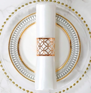 Detalle macro de servilletero oro rosa con diseño calado sobre satén blanco