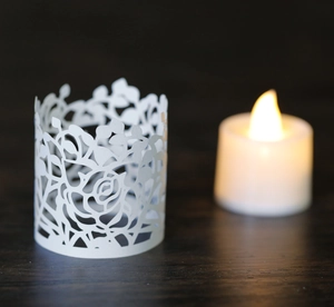 Detail of laser-cut white paper candle shades with intricate rose patterns on wood