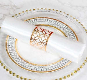 Detalle de un servilletero dorado calado con patrón geométrico en raso blanco