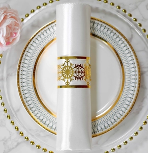 Close-up of golden snowflake napkin ring on white satin napkin and ceramic plate